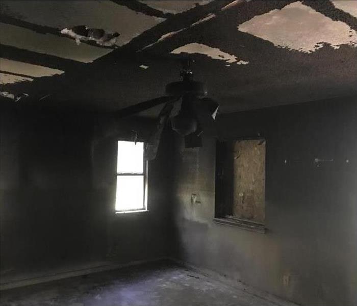 Interior of a building damaged by fire, one window boarded up, walls and ceiling covered with smoke